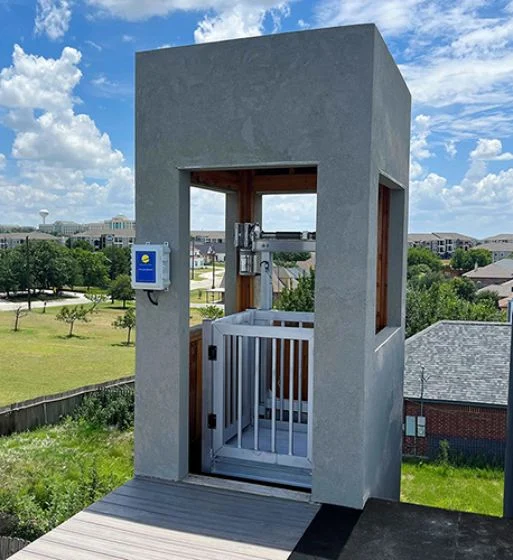 Outdoor home elevator with a gated platform against a rural backdrop, offering accessibility and convenience in a residential area.