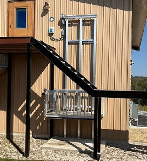 Exterior view of a beige building featuring a home elevator with a metal platform and rails, connected to a second-story door.