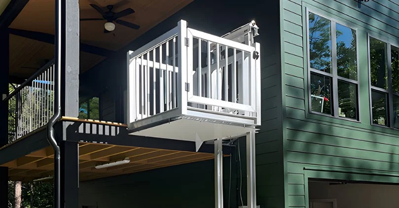 White home elevator attached to a modern green house exterior, connected to an elevated deck with black railing.